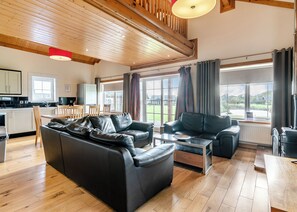 Amplia sala de estar con un sofá de cuero negro grande, un sofá más pequeño, una mesa de centro y un comedor con sillas y mesa de madera.