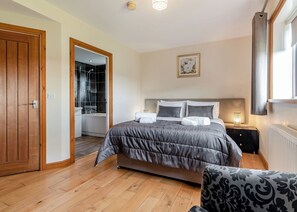 A bedroom with a bed, bedside table, nightstand, and a window with curtains.