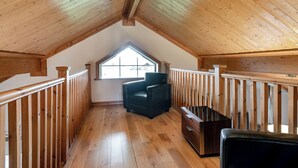 Una habitación de ático con techo inclinado, una ventana, una silla negra y un banco de madera.