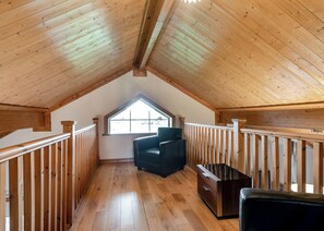 A wooden attic room with a sloped ceiling, a window, a black chair, and a wooden bench.