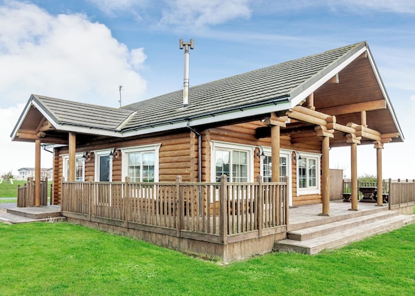 Eine Blockhütte mit Veranda, Schornstein und einem eingezäunten Deck.