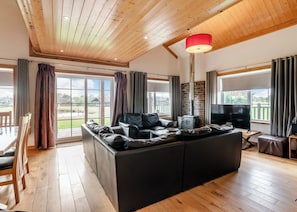 A spacious living room with a large black leather sofa, a TV, and a red lamp.