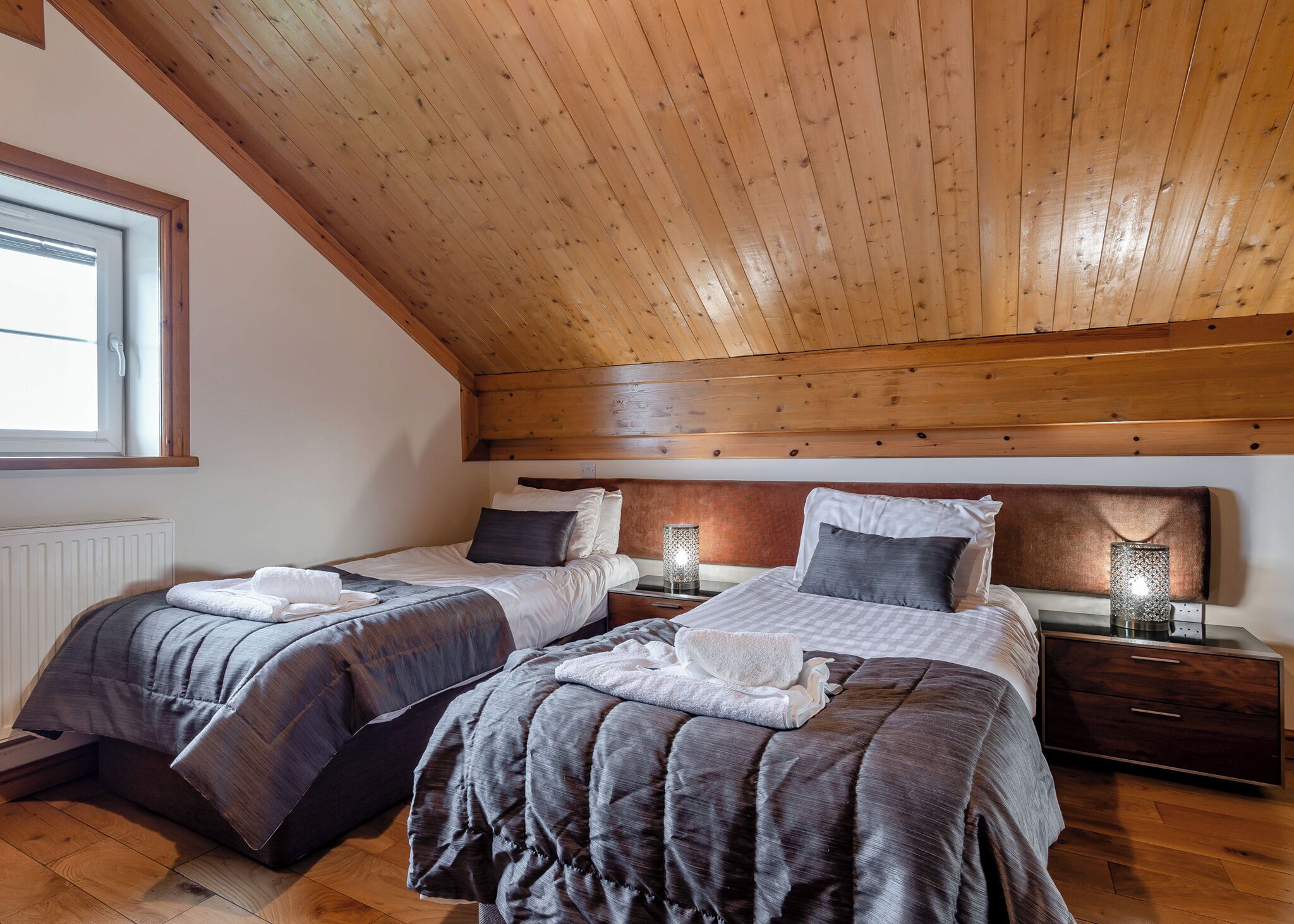 Une chambre avec deux lits, des poutres apparentes en bois au plafond, une fenêtre et des lampes de chevet.