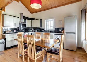 A modern kitchen with wooden cabinets, a dining table with chairs, a washing machine, and a refrigerator.