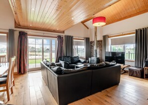 A spacious living room with a large black leather sofa, a TV, and a red lamp.