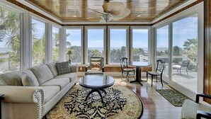 Una habitación amplia con un gran ventanal, ventilador de techo, sofá, mesa de centro y zona de comedor con sillas.