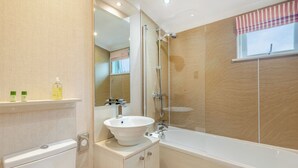 Un baño moderno con un lavabo blanco, ducha con cerramiento de vidrio y una ventana con cortinas a rayas.