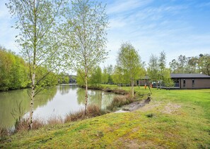 Un paisaje tranquilo junto al lago, con un pequeño muelle, zonas verdes y un edificio al fondo.