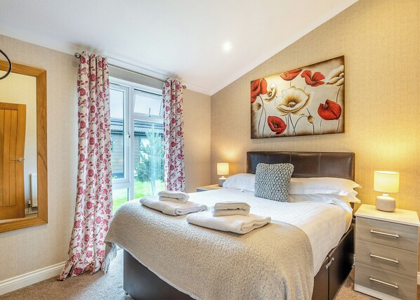 Een hotelkamer met een bed, nachtkastje, lamp, schilderij en een raam met gordijnen.