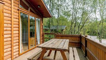 Une cabane en bois dotée d’une terrasse, de grandes fenêtres et offrant une vue sur la forêt environnante.
