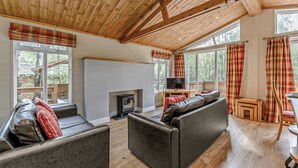 Ein geräumiges Wohnzimmer mit Kamin, großen Fenstern und einer hohen Holzbalkendecke.