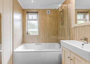 A bathroom with a bathtub, a shower, a vanity with a mirror, and a window.