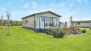 Una casa móvil moderna con un ventanal grande, una pequeña terraza y un jardín cuidado.