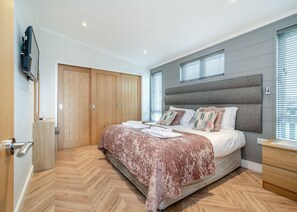 A bedroom with a bed, wooden wardrobe, and a TV mounted on the wall.