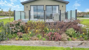Un edificio moderno con amplios ventanales, un área de estar al aire libre techada y un jardín bien cuidado con diversas plantas y flores.