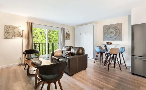 A modern living room with a sofa, chairs, a dining table, and a balcony with a view. - Beautifully Remodeled Top-Floor Condo Downtown! (Bend)