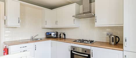 A modern kitchen with white cabinets, a gas stove, a microwave, and a stainless steel kettle.