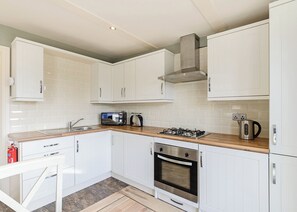 Una cocina moderna con armarios blancos, estufa a gas, microondas y hervidor de acero inoxidable.