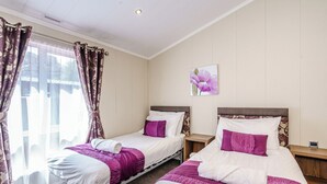 Une chambre d’hôtel avec deux lits, une fenêtre avec des rideaux, une table de chevet et un tableau représentant des fleurs accroché au mur.