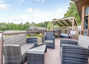 A covered outdoor seating area with wicker furniture, a barbecue grill, and a wooden deck.