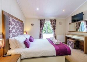 A bedroom with a bed, a desk, a TV, and a window with curtains.