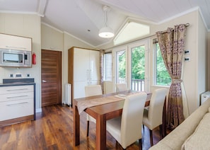 A dining area with a wooden table and chairs, a microwave, and a view of greenery through large windows.