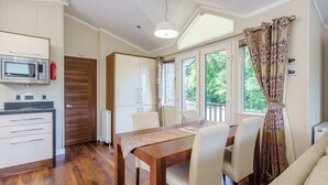 Un coin repas avec une table et des chaises en bois, un four à micro-ondes et une vue sur la verdure grâce à de grandes fenêtres.