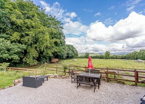A patio area with a wooden fence, outdoor seating, and a view of a green field and trees.