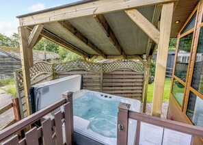 A wooden deck with a hot tub, a covered area, and a wooden fence.