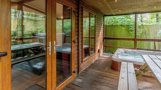 Un espace extérieur abrité doté d’un plancher en bois, de portes vitrées, d’un jacuzzi et d’une table de pique-nique.