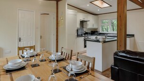 Un coin repas avec une table en bois dressée pour quatre personnes, une cuisine en arrière-plan et une fenêtre donnant sur des arbres.