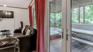 Une pièce équipée d’un téléviseur, d’un canapé, d’un jacuzzi et d’une porte-fenêtre coulissante donnant sur un espace extérieur.