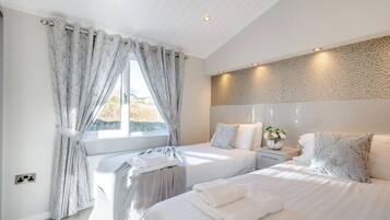 A modern bedroom with two beds, a large window with curtains, a stone-textured wall, and a bedside table with a vase.