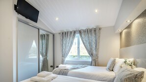 A bedroom with two beds, a TV mounted on the wall, and a window with curtains. - 1 bedroom accommodation in Dumfries, Dumfries & Galloway (Dumfries, Dumfries & Galloway)
