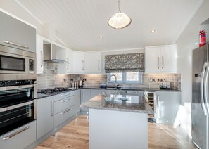 A modern kitchen with stainless steel appliances, white cabinetry, a central island, and a large window.