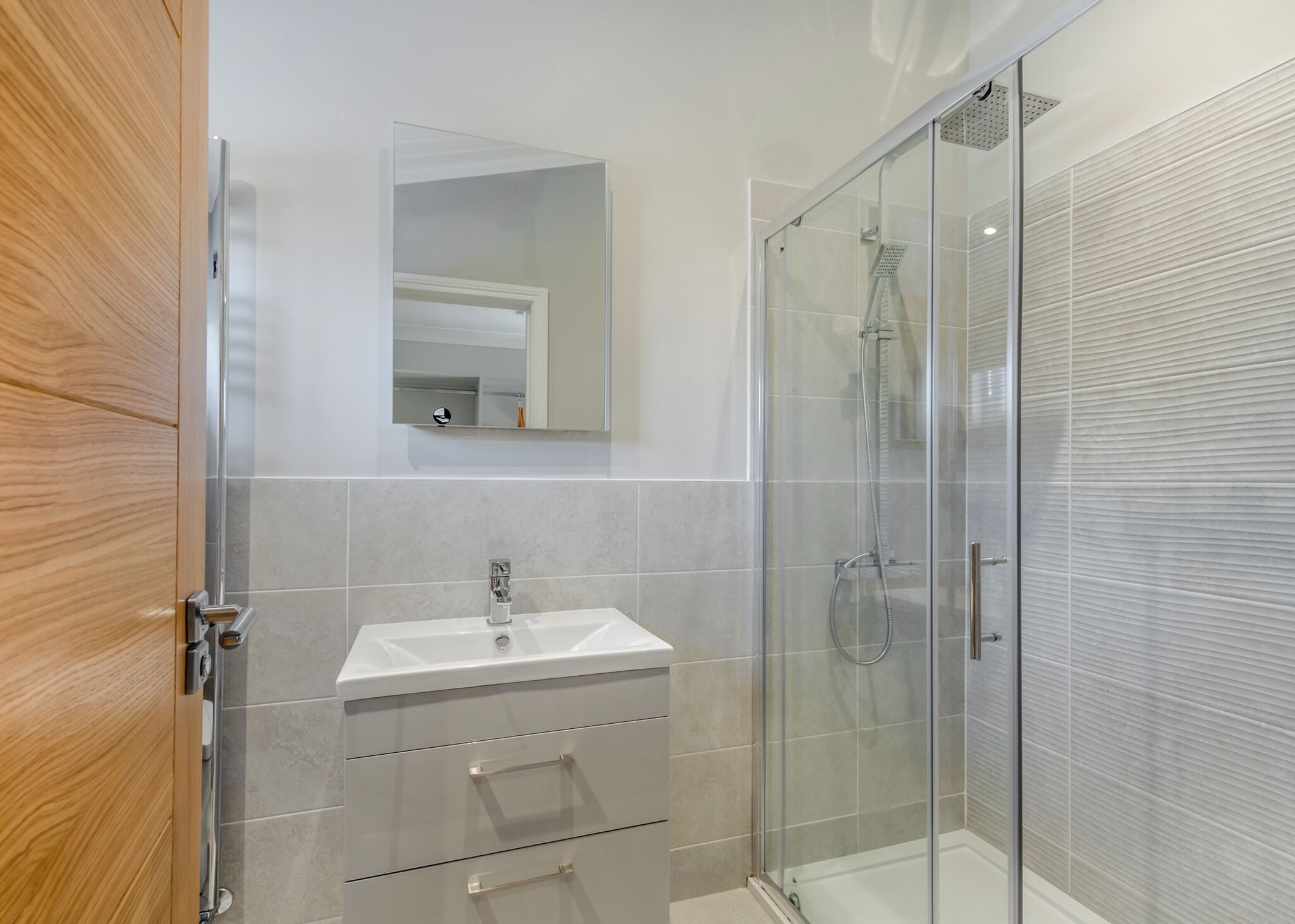 A modern bathroom with a glass shower enclosure, a white sink, and a wooden door.