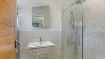 A modern bathroom with a glass shower enclosure, a white sink, and a wooden door.