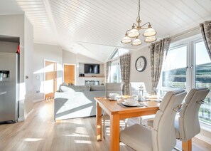A modern kitchen with a built-in oven, a dining area with a wooden table and chairs, a sofa, and a large window with curtains.