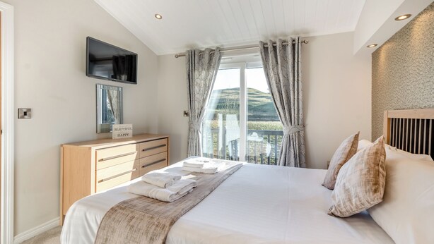 A bedroom with a bed, a TV mounted on the wall, a wooden dresser, and a window with curtains. - 1 bedroom accommodation in Dumfries, Dumfries & Galloway (Dumfries, Dumfries & Galloway)
