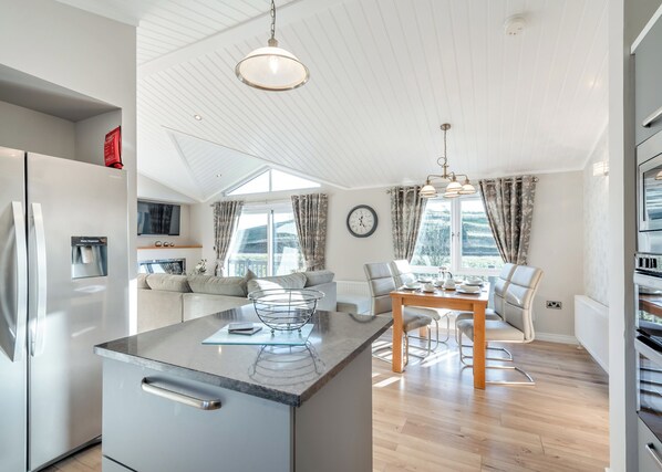 A modern kitchen with a built-in water dispenser, a dining area with a wooden table and chairs, and a large window with curtains.