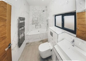 A modern bathroom with a toilet, sink, shower, and a wooden door.