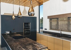 A modern kitchen with a central island, built-in oven, and pendant lighting.