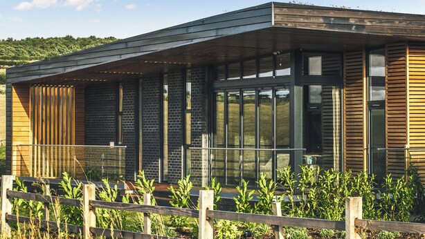 A modern building with large windows, a wooden fence, and a grassy area. - Two bed lodge with one king-size bed and one twin (King by arrangement). (Nottingham)