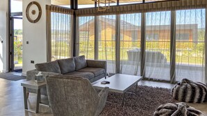 Un salon moderne avec un canapé, une table basse et un fauteuil, de grandes fenêtres et un plancher en bois.
