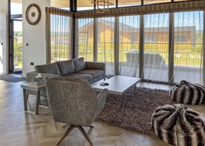 A modern living room with a sofa, coffee table, and armchair, large windows, and a wooden floor. - Two bed lodge with one king-size bed and one twin (King by arrangement). (Nottingham)