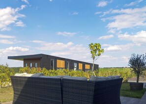 A modern house with a flat roof, large windows, and a garden with wicker furniture.