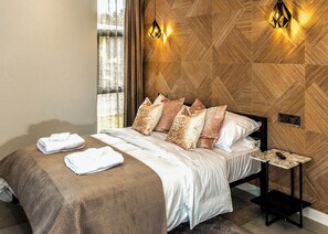 A hotel room with a bed, pillows, a nightstand, and a wall-mounted light fixture.