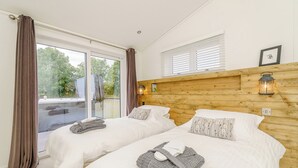 A bedroom with two beds, a wooden headboard, a window with blinds, and a lantern on the wall.