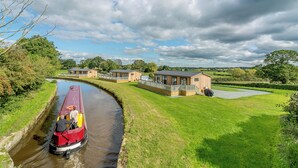 A canal-side property with a boat, wooden buildings, and a grassy landscape.