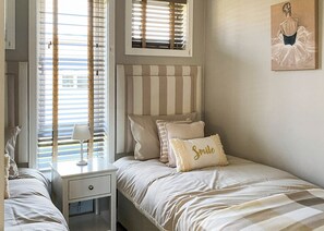 A bedroom with a striped headboard, a bedside table with a lamp, and a pillow with the word 'Smile'.